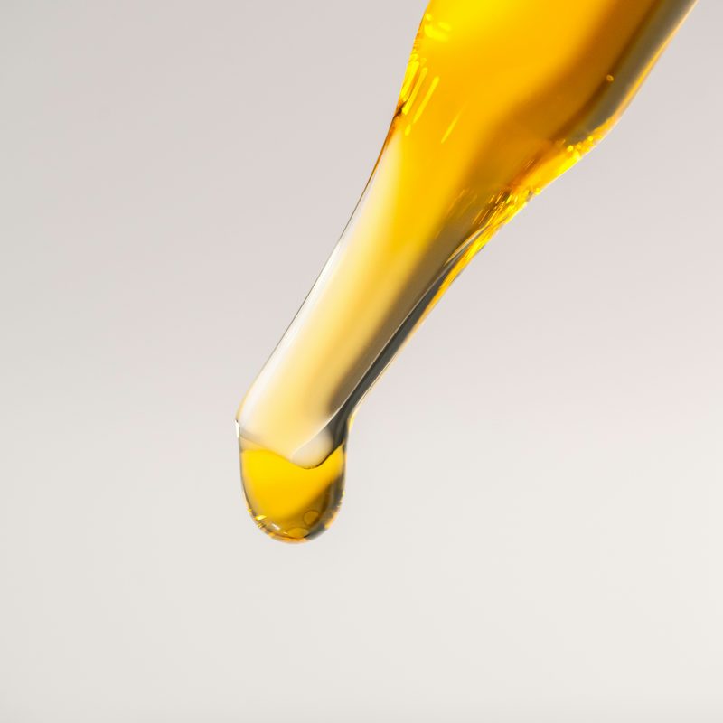 Golden jojoba oil dropping from a pipette
